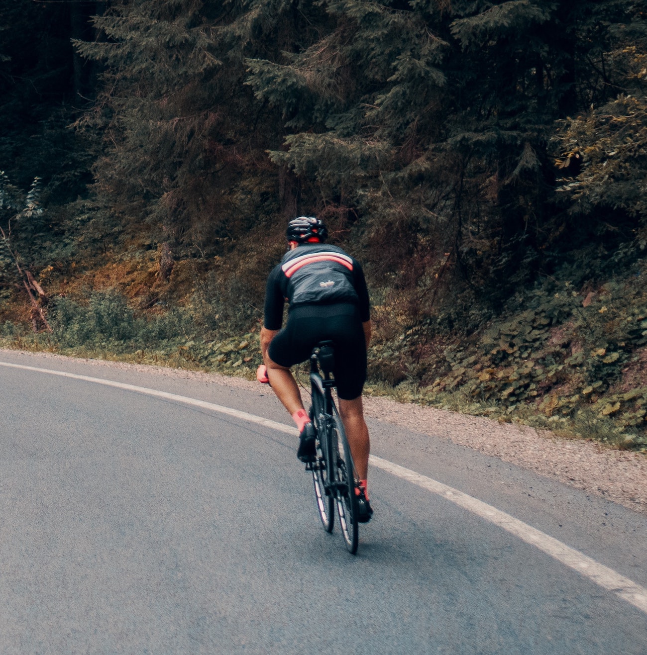 Man in all black biking along the side of a road along a curve.