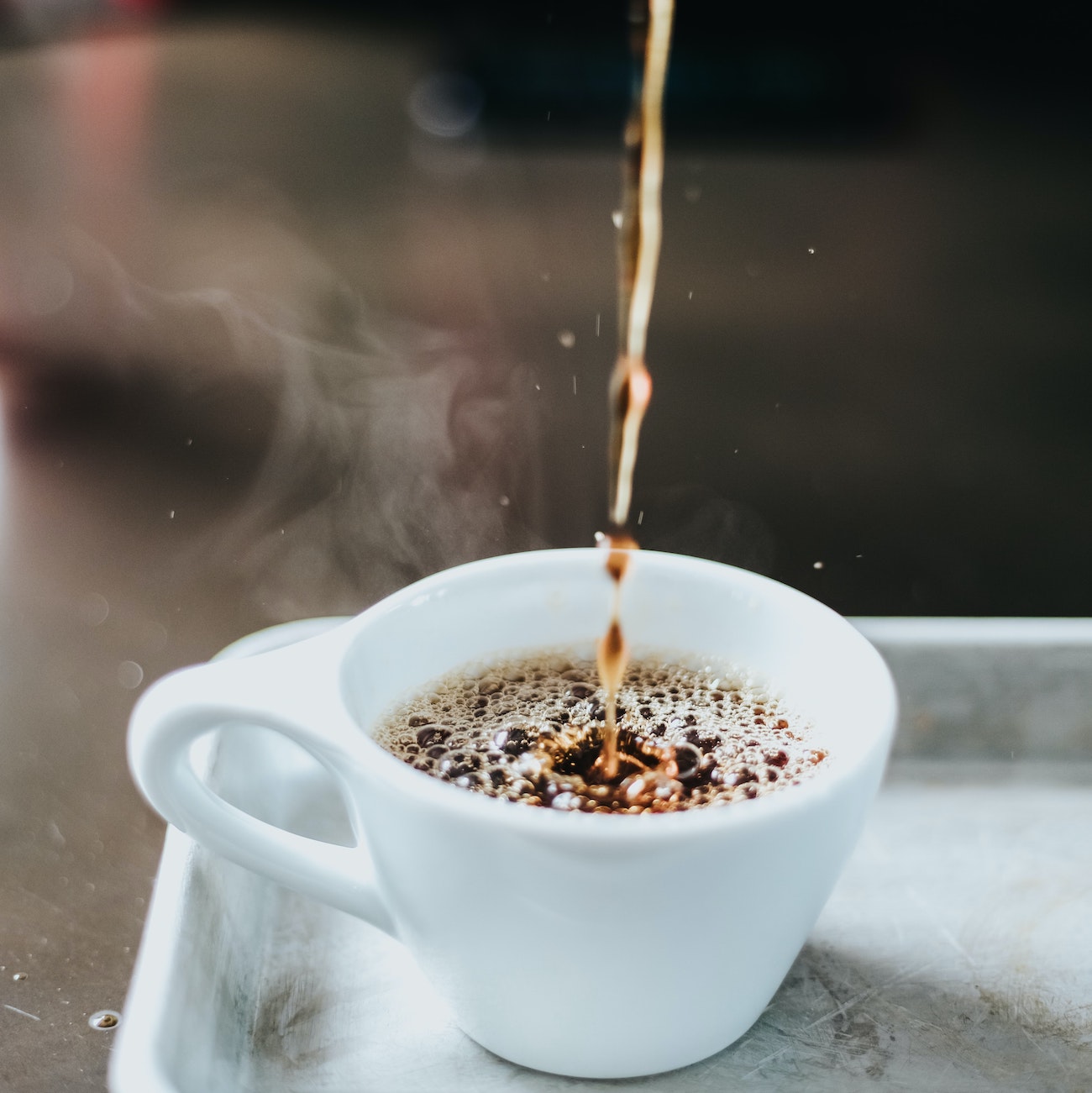 Steaming hot coffee being poured into a white coffee cup sitting on a tray.