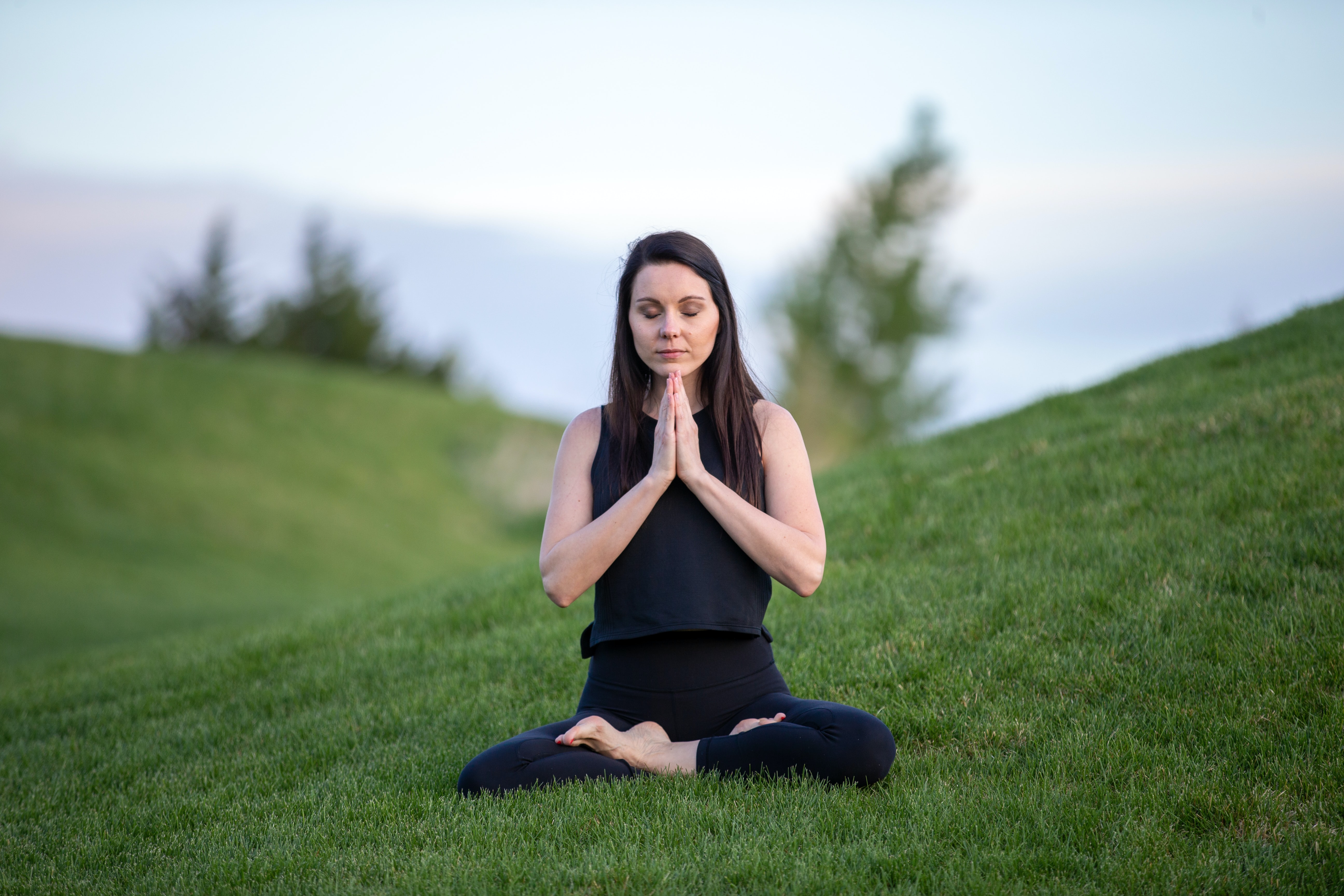 Woman meditating in field with crossed legs and prayer hands.