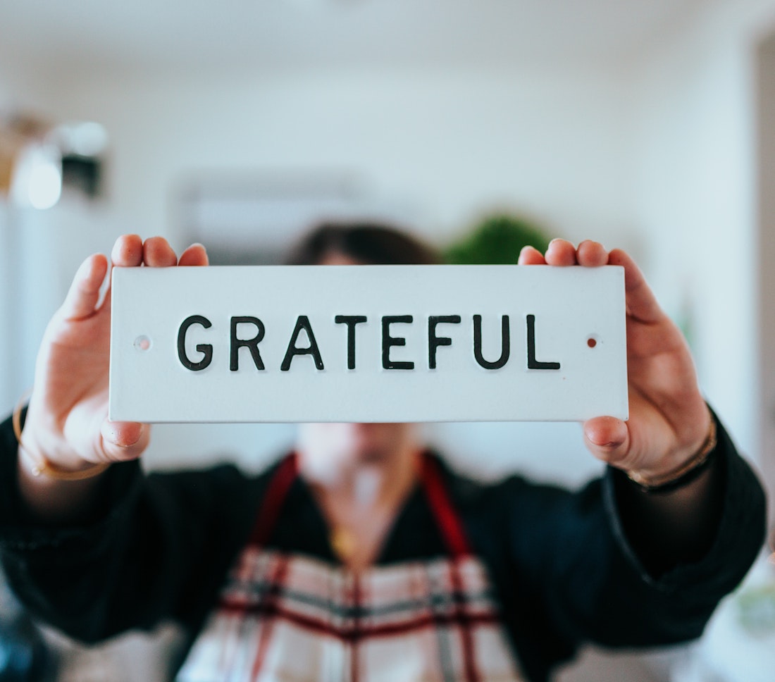 A blurred person holding a rectangular wooden sign up to the camera that says Gratitude.