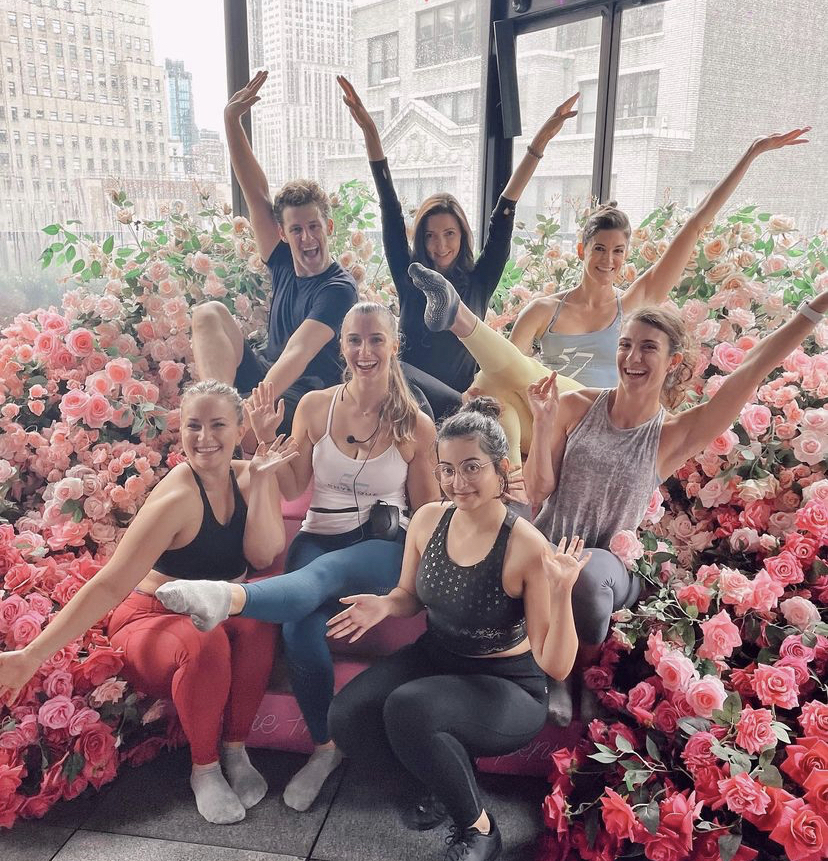 A group of Physique 57 barre instructors smiling at the camera in front of a floral wonderland during the Inspiring Strength Tour